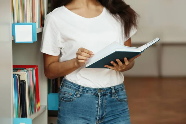 Jeune femme avec livre près d'une étagère à la bibliothèque, gros plan — Photo