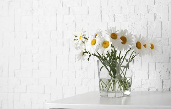 Hermosas flores tiernas de manzanilla en jarrón en inodoro de madera cerca de la pared de textura blanca, espacio para el texto — Foto de Stock