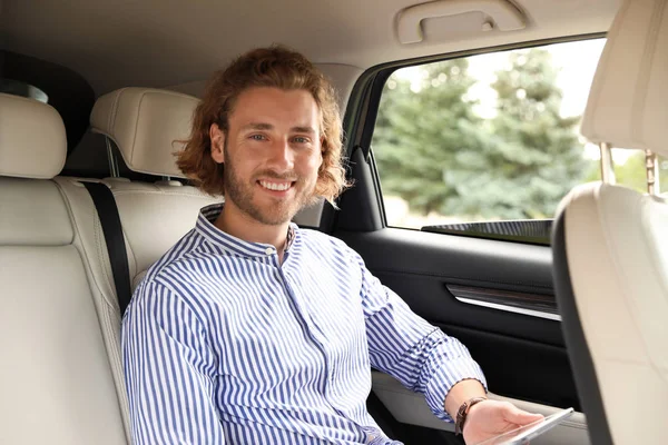 Vonzó fiatal férfi tabletta a hátsó ülésen a luxusautó — Stock Fotó