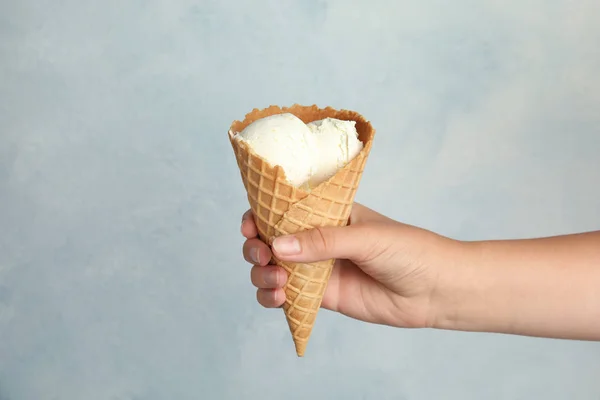Mujer sosteniendo delicioso helado en cono de oblea sobre fondo azul claro, primer plano — Foto de Stock