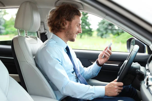 Jeune homme attrayant utilisant le téléphone tout en conduisant sa voiture de luxe — Photo