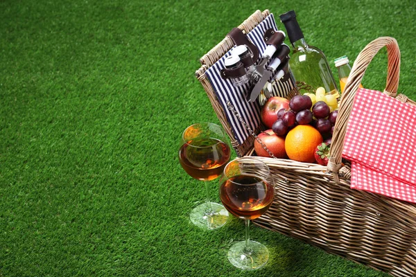Wiklinowy kosz piknikowy z różnymi produktami na zielonej trawie, miejsce na tekst — Zdjęcie stockowe