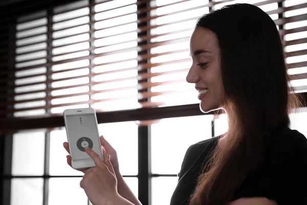 Mulher usando o aplicativo casa inteligente no telefone para controlar persianas dentro de casa — Fotografia de Stock