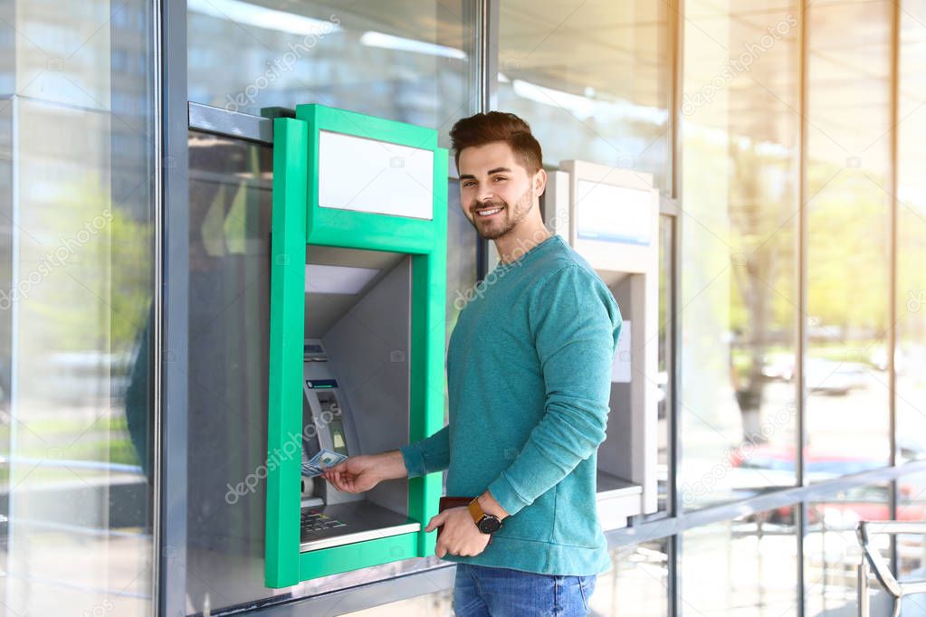 Young man taking money from cash machine outdoors