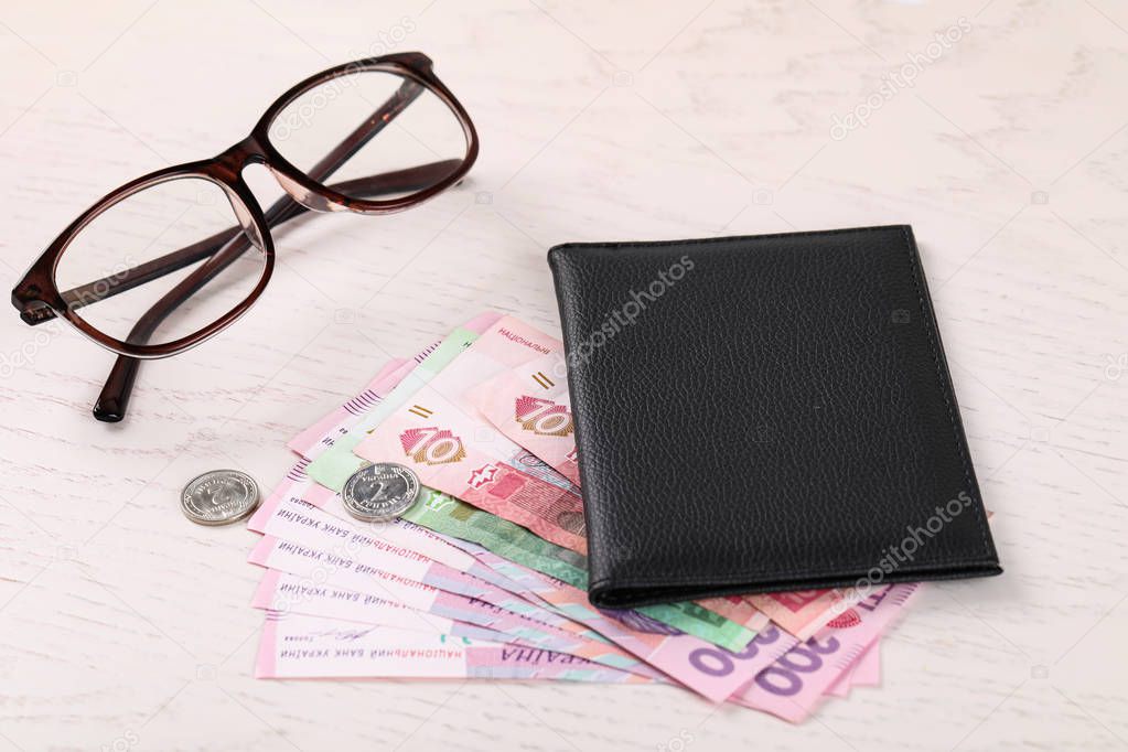 Pension certificate with Ukrainian money and glasses on white wooden background