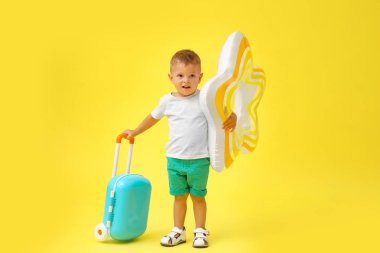 Sarı arka plan üzerinde şişme yüzük ve mavi bavul ile Sevimli küçük çocuk