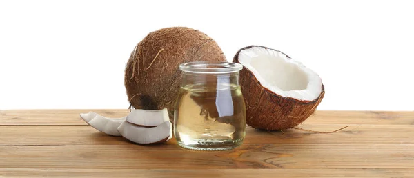 Cocos maduros e jarra com óleo orgânico natural sobre mesa de madeira contra fundo branco — Fotografia de Stock