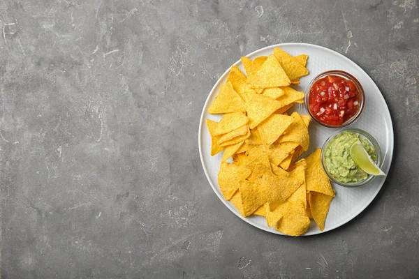 Plate with delicious mexican nachos chips and sauces on grey table, top view. Space for text — Stock Photo, Image