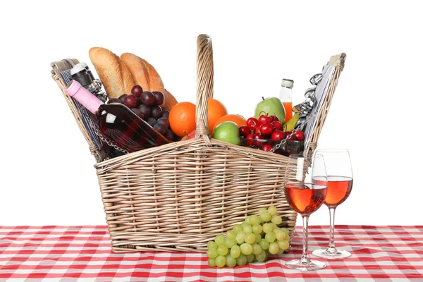 Wicker picnic basket with different products on checkered tablecloth against white background — Stock Photo, Image