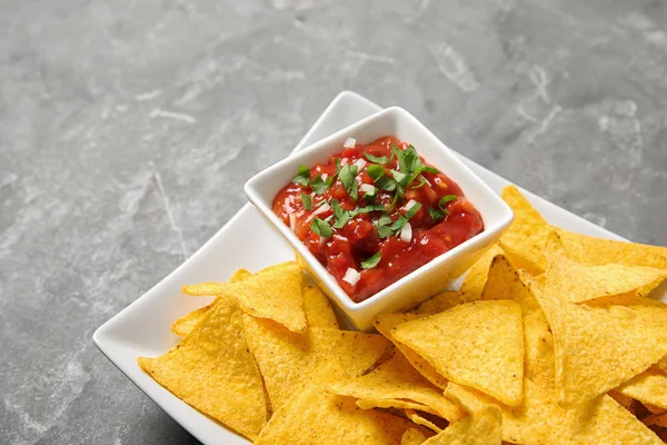 Plate with delicious mexican nachos chips and salsa sauce on grey table, closeup — Stock Photo, Image