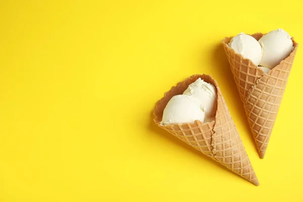 Delicioso sorvete de baunilha em cones wafer no fundo amarelo, flat lay. Espaço para texto — Fotografia de Stock