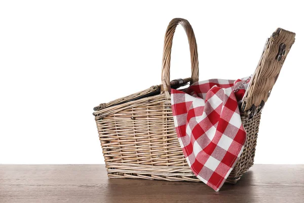 Wicker picnic basket and checkered blanket on wooden table against white background — Stock Photo, Image