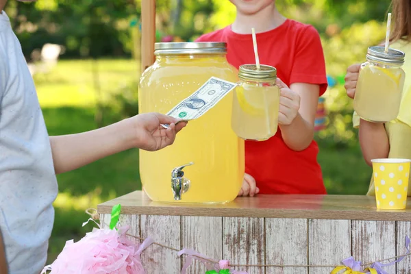 Kleine Mädchen verkaufen natürliche Limonade an Jungen im Park, Nahaufnahme. Erfrischungsgetränk im Sommer — Stockfoto