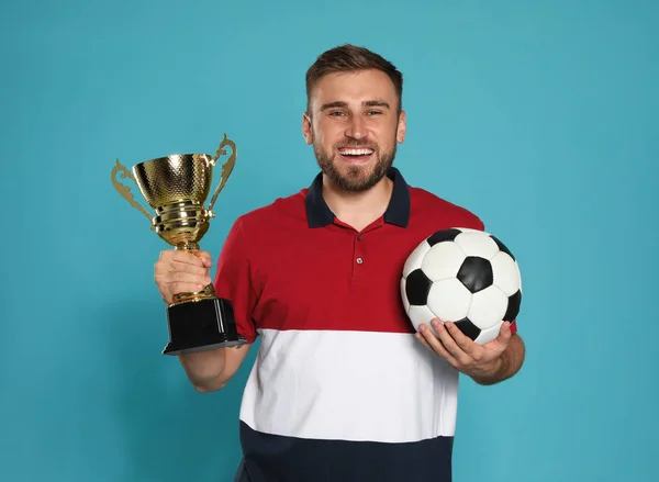 Retrato de jovem jogador de futebol feliz com copo de troféu de ouro e bola no fundo azul — Fotografia de Stock