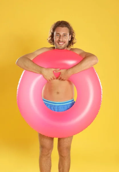 Atractivo joven en ropa de playa con anillo inflable rosa sobre fondo amarillo — Foto de Stock