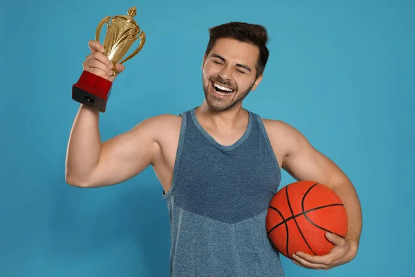 Portrait of happy young basketball player with gold trophy cup on blue background