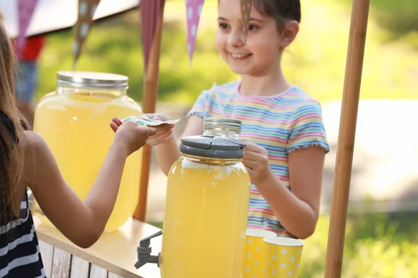 Kleines Mädchen verkauft natürliche Limonade an Kinder im Park. Erfrischungsgetränk im Sommer — Stockfoto