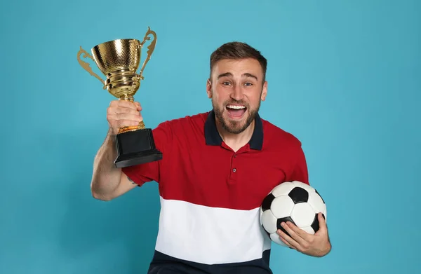 Retrato de jovem jogador de futebol feliz com copo de troféu de ouro e bola no fundo azul — Fotografia de Stock