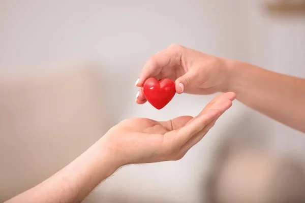 Γυναίκα που δίνει κόκκινη καρδιά στον άνθρωπο σε θολή φόντο, κοντινό. Ιδέα δωρεάς — Φωτογραφία Αρχείου