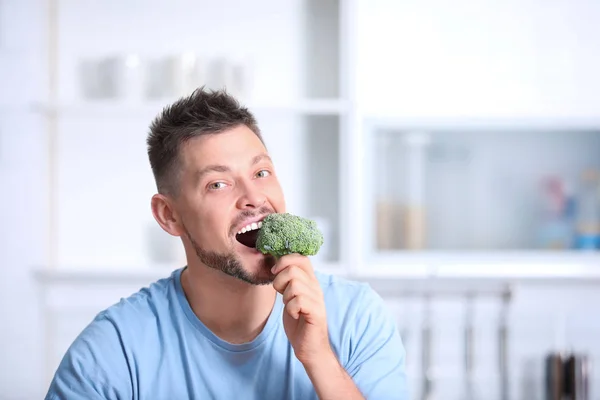 Portrait of happy man eating broccoli in kitchen