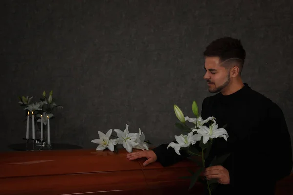 Sad young man with white lilies near casket in funeral home — Stock Photo, Image