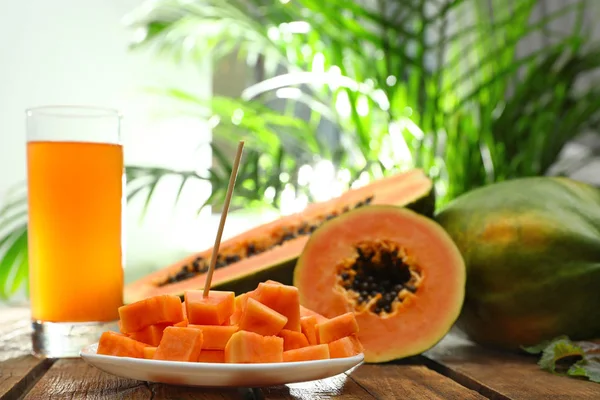 Fresh papayas and juice on wooden table against blurred background, space for text