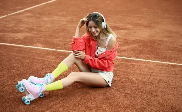 Feliz mujer joven con estilo con patines de ruedas vintage y auriculares sentados en la cancha de tenis —  Fotos de Stock