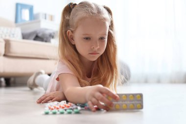 Evde yerde farklı hapları olan küçük bir çocuk. Ev seli tehlikesi