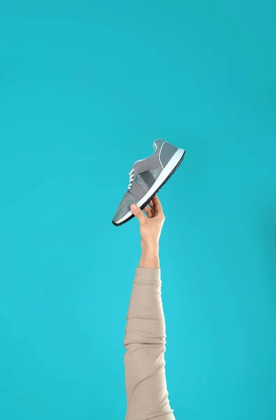 Hombre joven sosteniendo zapato cómodo sobre fondo azul claro, primer plano — Foto de Stock