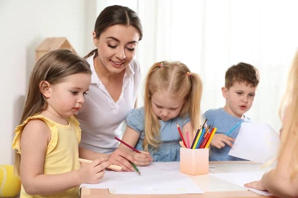 Маленькие дети с воспитателем детского сада рисуют за столом в помещении. Обучение и игры — стоковое фото