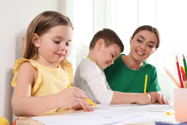 Niños pequeños con maestra de jardín de infantes dibujando en la mesa en el interior. Aprender y jugar — Foto de Stock