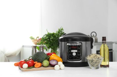 Modern multi cooker and products on table in kitchen. Space for text clipart