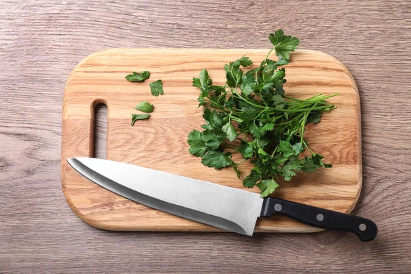 Доска с ножом шеф-повара и свежей петрушкой на деревянном столе, вид сверху — стоковое фото