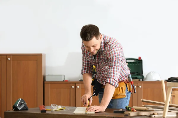 Snygg arbets man gör märken på timmer vid bordet inomhus. Hem reparation — Stockfoto