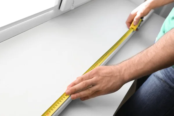 Мужчина измеряет белый подоконник в помещении, крупным планом. Строительный инструмент — стоковое фото