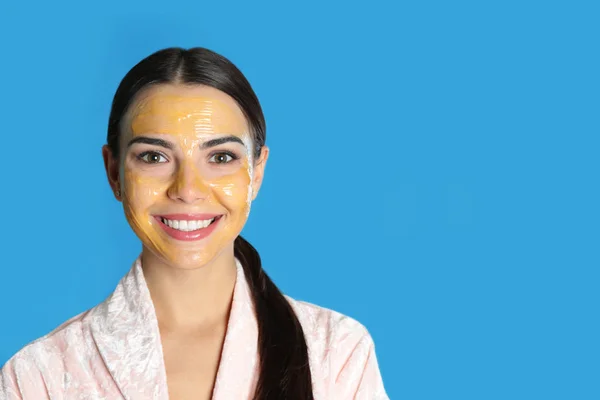 Young woman with cleansing mask on her face against color background, space for text. Skin care