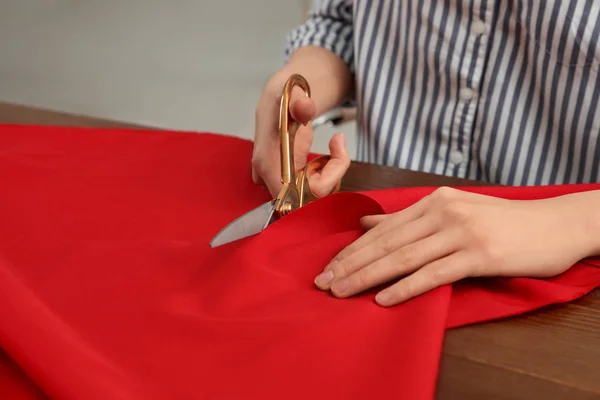 Жінка ріже тканину з гострими ножицями за дерев'яним столом, крупним планом. Простір для тексту — стокове фото