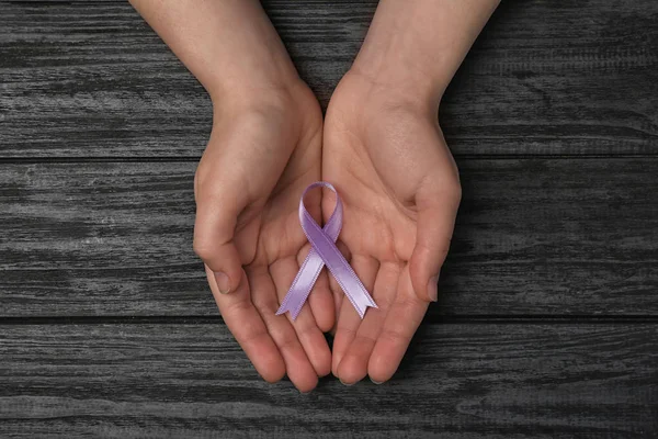 Vrouw Holding paarse bewustzijn lint op zwarte houten achtergrond, Top View — Stockfoto