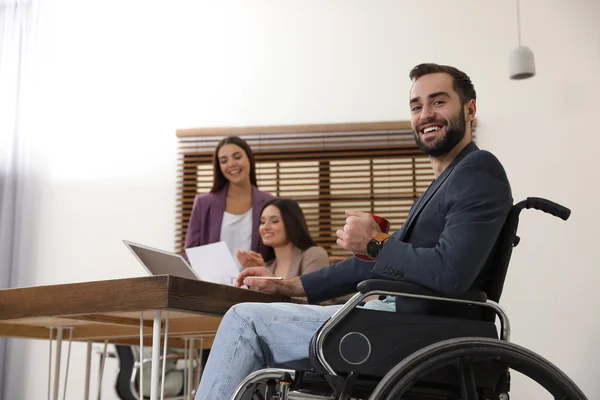 Jovem em cadeira de rodas com colegas no local de trabalho — Fotografia de Stock