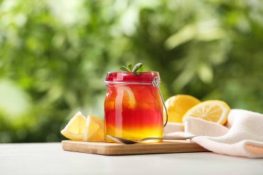 Beyaz masada renkli jöle, kaşık ve limon dilimleri kavanoz ile Board