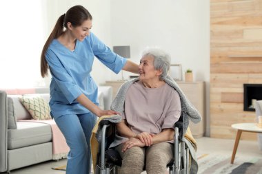 Hemşire kapalı battaniye ile tekerlekli sandalyede yaşlı kadın kapsayan. Kıdemli kişilere yardımcı olmak