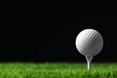 Siyah arka plana karşı suni çim üzerinde tee ile golf topu, metin için alan