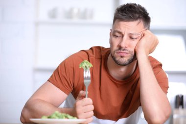 Mutfakta brokoli salatası yiyen mutsuz adamın portresi
