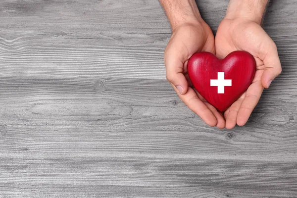 Hombre sosteniendo el corazón rojo sobre fondo de madera, vista superior con espacio para el texto. Concepto de donación —  Fotos de Stock