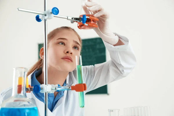 Alumno inteligente mirando frasco con reactivo en el soporte en la clase de química —  Fotos de Stock