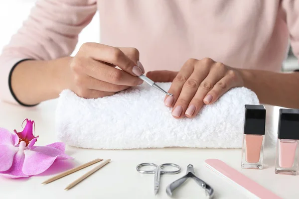 Woman removing fingernail cuticles at table, closeup. At-home manicure