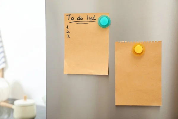 Hacer la lista y la hoja vacía del papel con los imanes a la puerta del refrigerador en la cocina. Espacio para texto — Foto de Stock