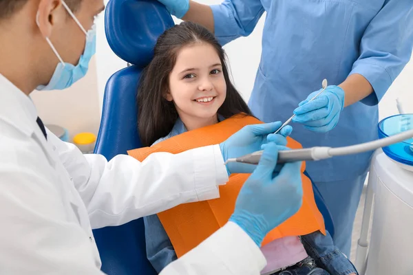 Professional dentist and assistant working with little girl in clinic — Stock Photo, Image