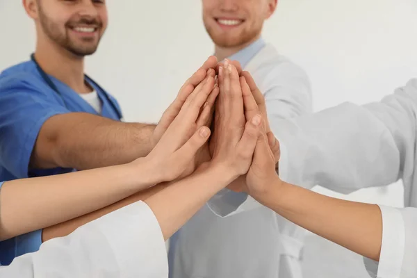 Equipo de trabajadores médicos tomados de la mano sobre fondo claro, primer plano. Concepto de unidad — Foto de Stock