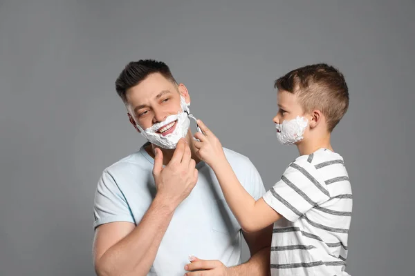 Zoon het scheren van zijn vader met scheermes op grijze achtergrond — Stockfoto